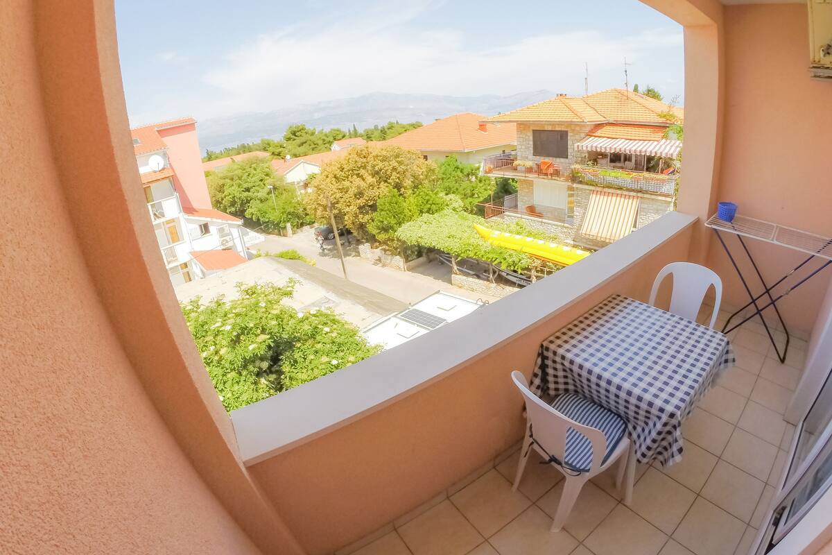 A balcony with a table and chairs, a view of a residential area, and a distant mountain range.
