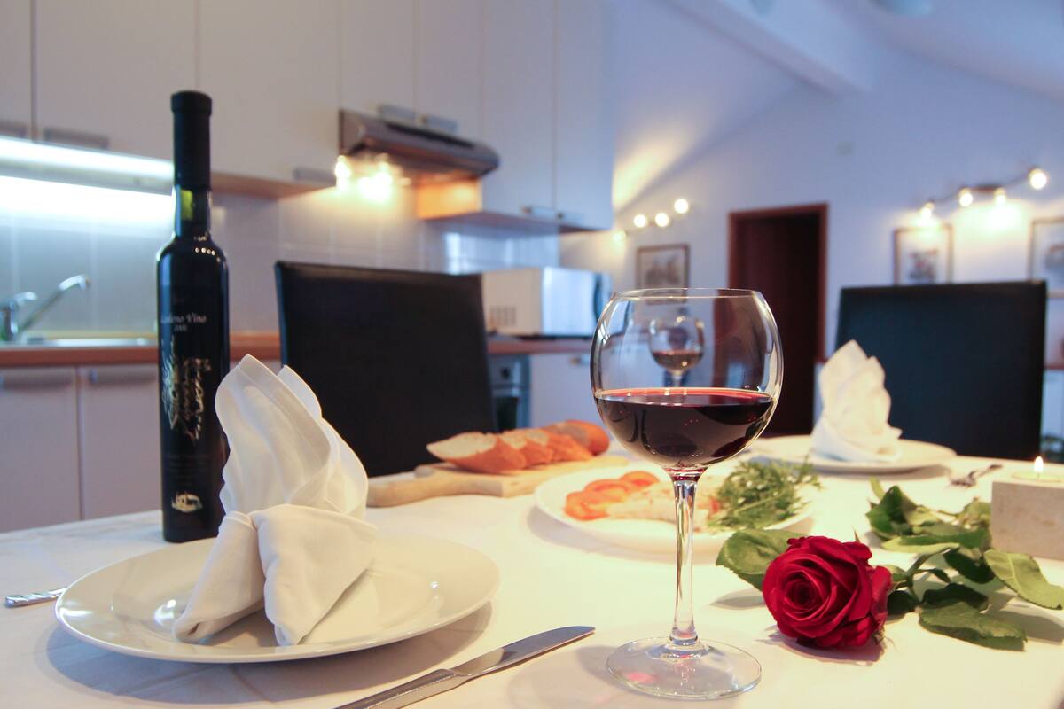 A dining table with a bottle of wine, a glass of red wine, a rose, and plates with food.