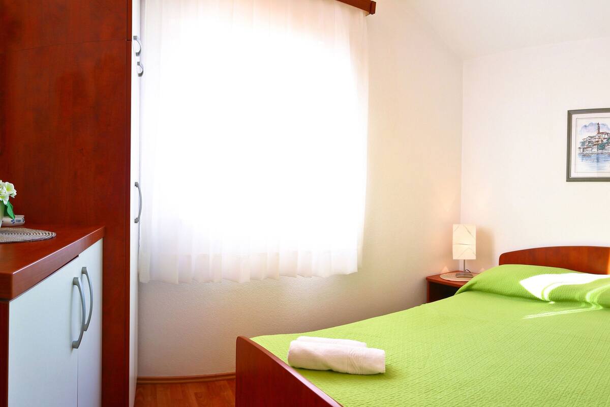 A hotel room with a bed, a nightstand with lamps, a small table with a vase of flowers, and a framed picture on the wall.