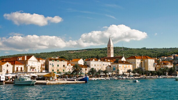 A coastal town with historic buildings, a prominent tower, and a marina with boats.