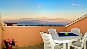 A round table with four chairs on a balcony, overlooking a mountainous landscape.