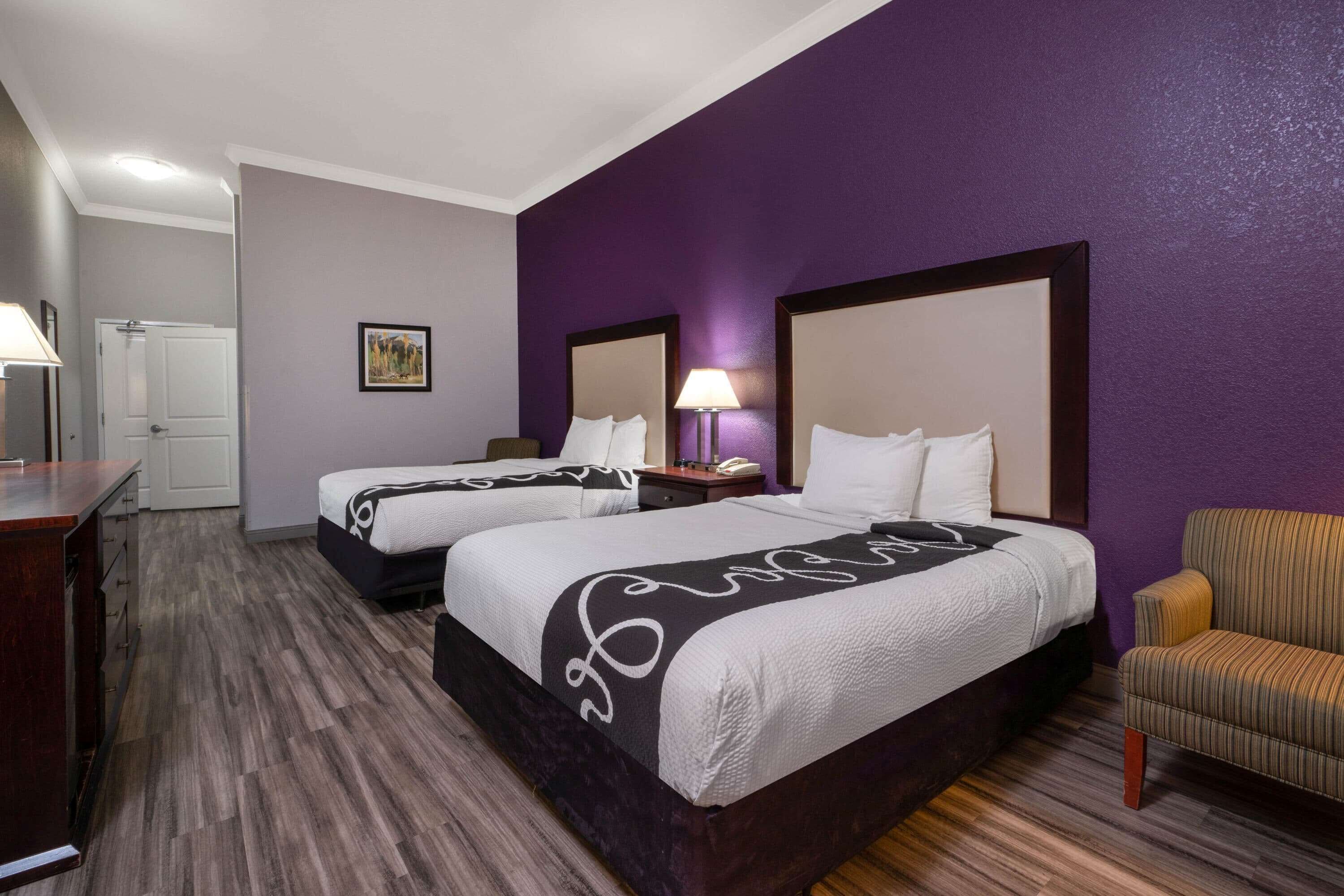 A hotel room with two beds, a desk, a chair, and a door.