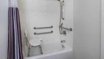 A bathroom with a white bathtub, grab bars, a shower chair, and a handheld showerhead.