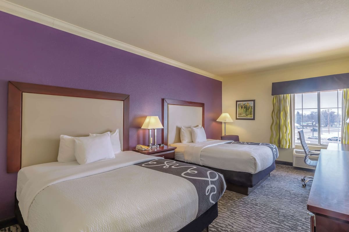 A hotel room with two beds, a desk, and a chair.
