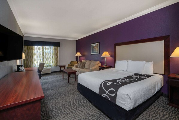 A hotel room with a large bed, a desk, a chair, and a television.