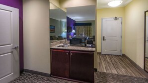 Habitación de hotel con kitchenette, un espejo grande, un lavamanos y una puerta que da a otra habitación.