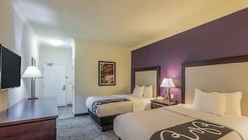 A hotel room with two beds, a desk, a TV, and a door leading to a hallway.
