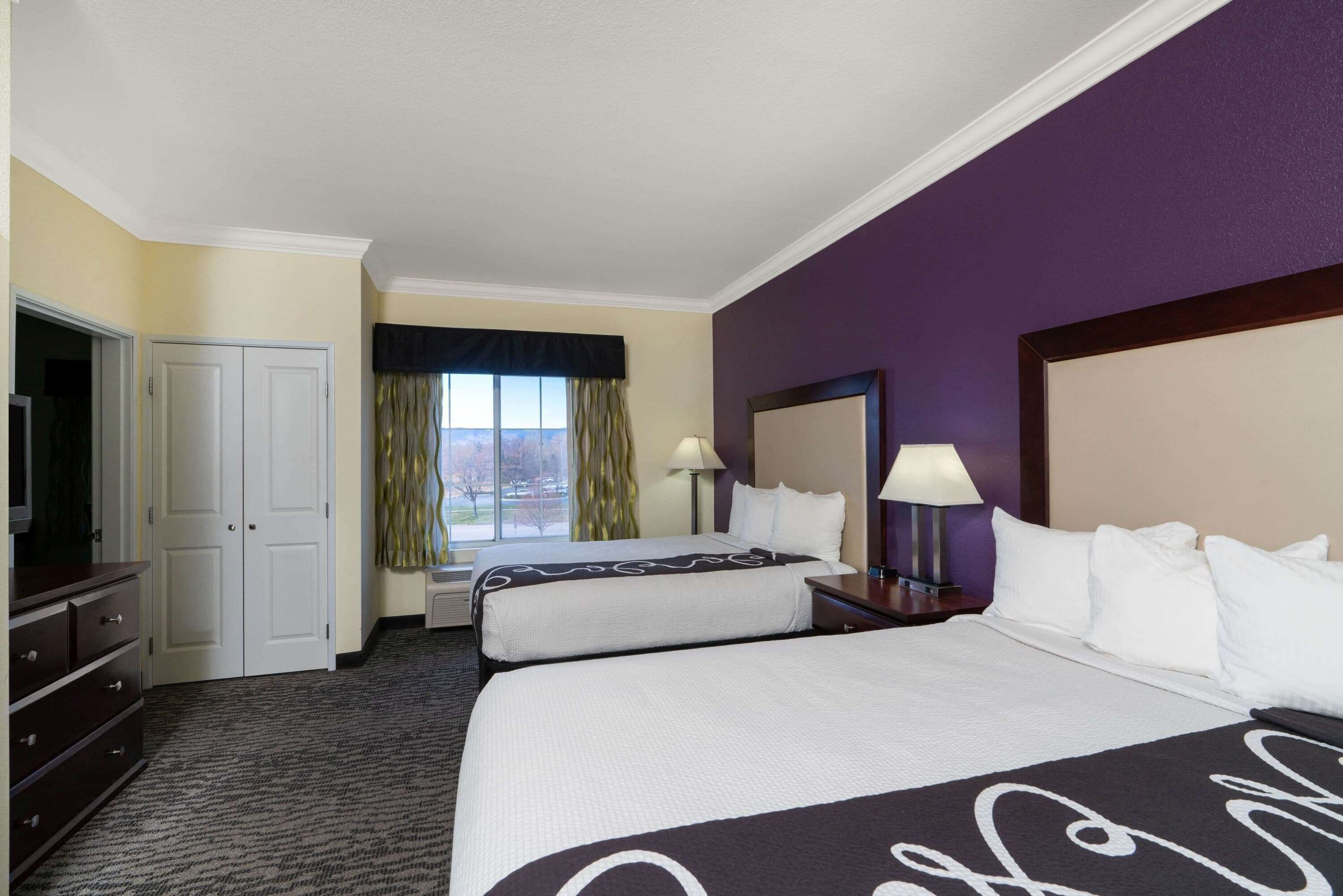 A hotel room with two beds, a desk, a TV, and a window with curtains.