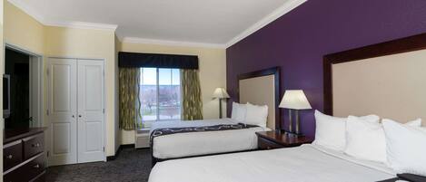 A hotel room with two beds, a desk, a TV, and a window with curtains.