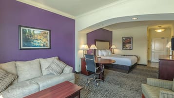 Une chambre d’hôtel avec un mur violet, un lit, un bureau, une chaise et un canapé.