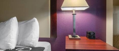 A hotel room with a bed, a nightstand, a lamp, and a digital clock.