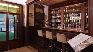 A bar area with wooden shelves stocked with liquor bottles, three bar stools, and a menu on the counter. - Recó de Randa (Algaida)