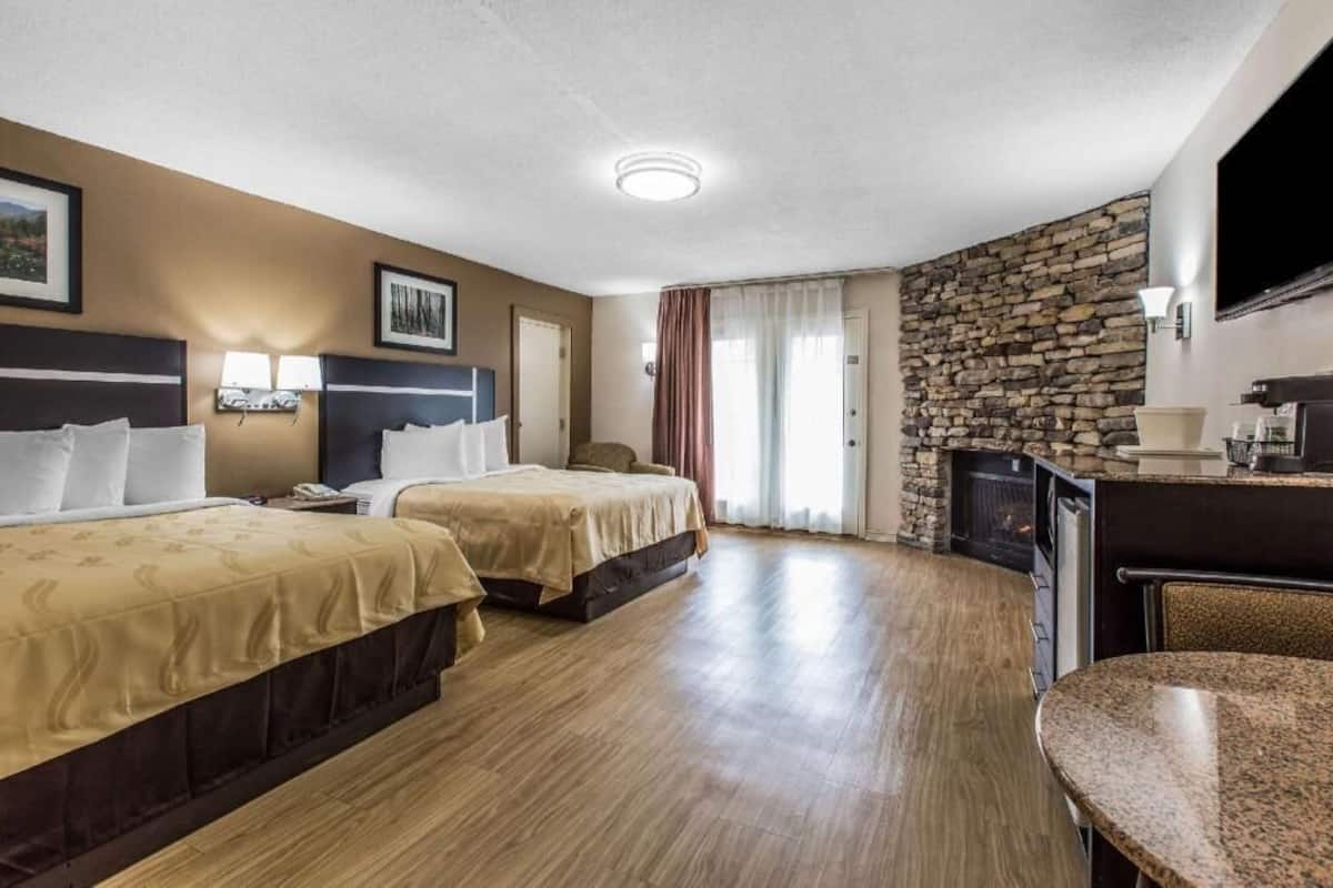 A hotel room with two beds, a stone wall, a flat-screen TV, and a small kitchenette.