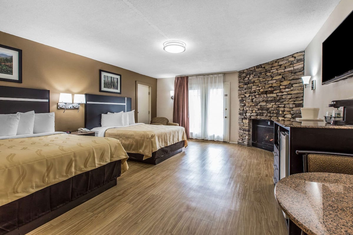 A hotel room with two beds, a stone fireplace, a TV, and a dining area.