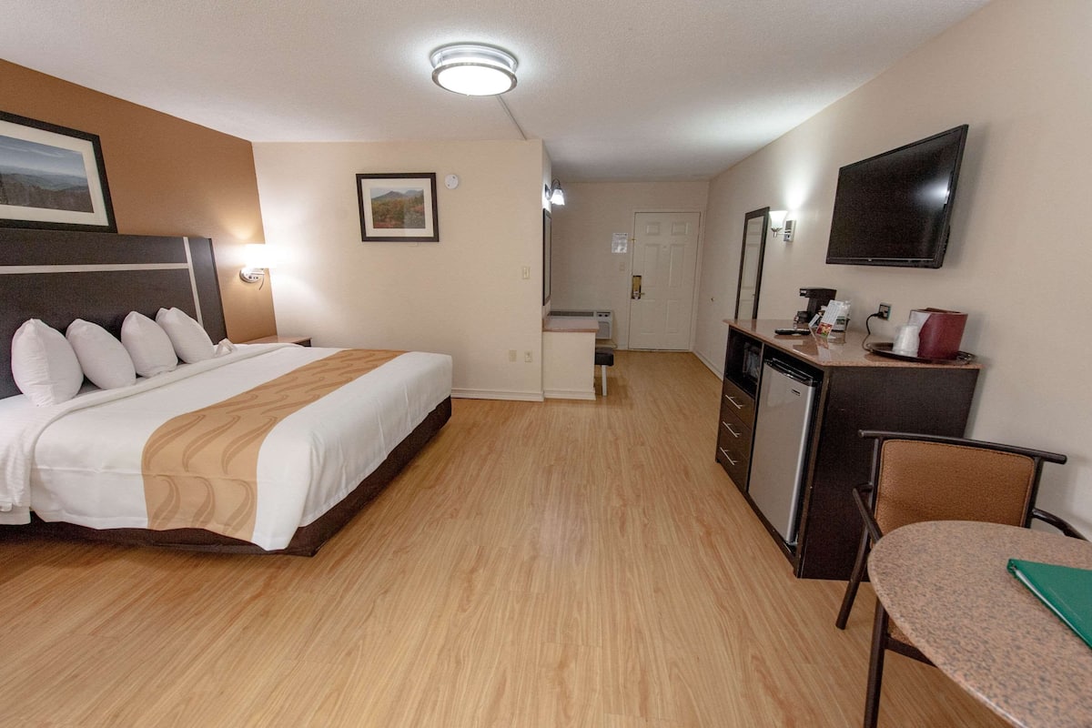 A hotel room with a bed, a desk, a chair, a TV, and a small kitchenette.