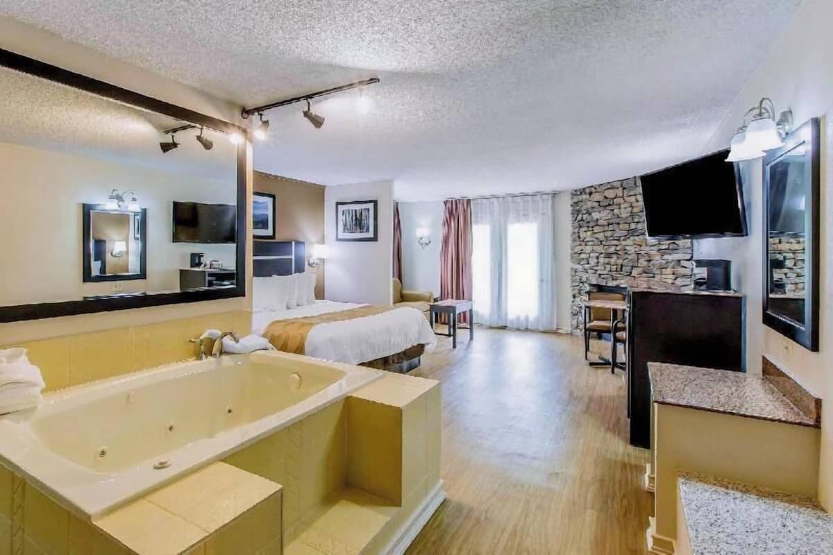 A hotel room with a large bathtub, a bed, a desk, and a television.
