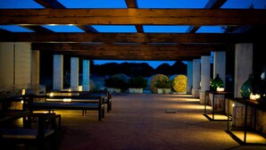 Un espace extérieur couvert, aménagé en patio, avec des poutres en bois, des bancs et des tables.