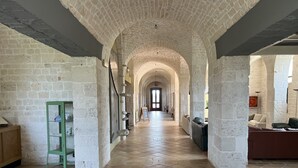 Un vaste couloir au plafond haut et aux murs en briques apparentes, qui mène à une porte au fond.