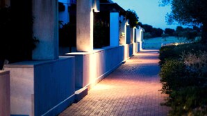 Un chemin bordé de colonnes et éclairé d’une lumière chaleureuse, menant à un bâtiment au style architectural moderne.