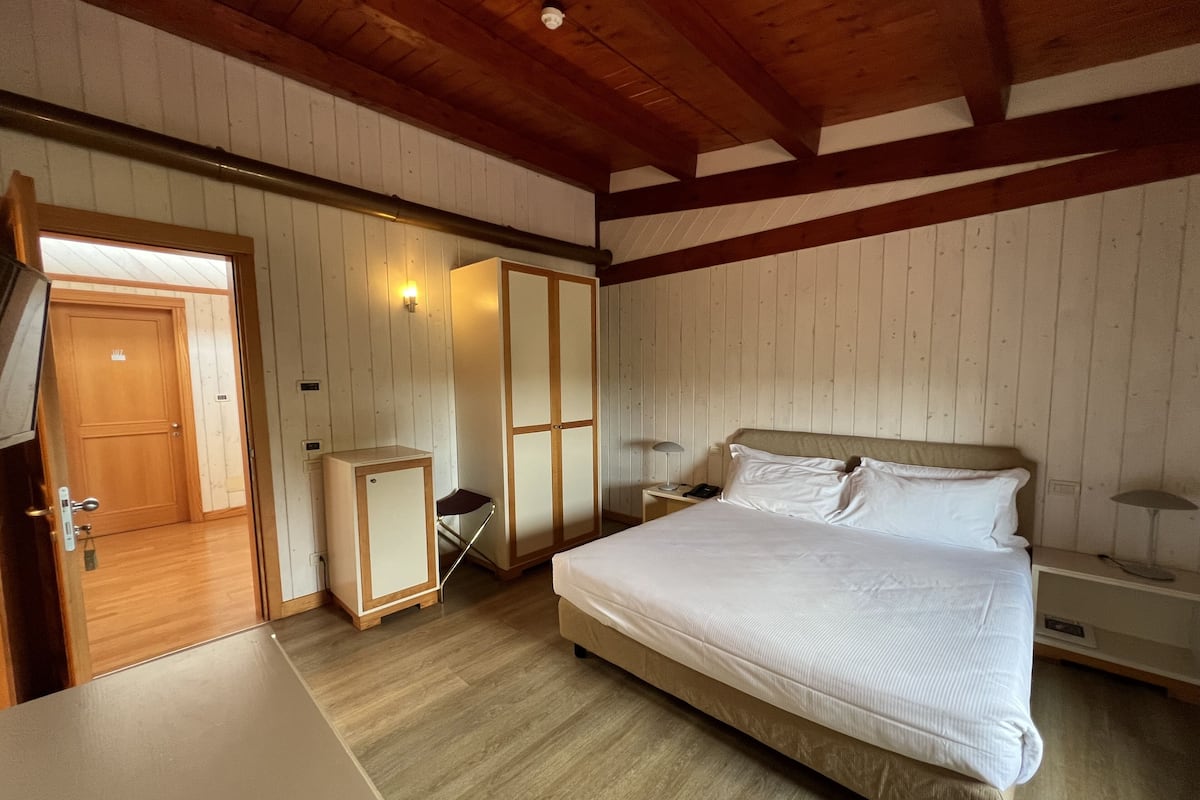A bedroom with a wooden ceiling, a bed with white linens, a nightstand, and a wardrobe.