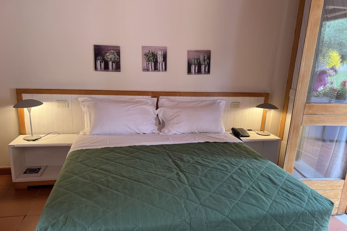 A neatly made bed with a green quilt, two bedside tables with lamps, and three framed pictures on the wall.
