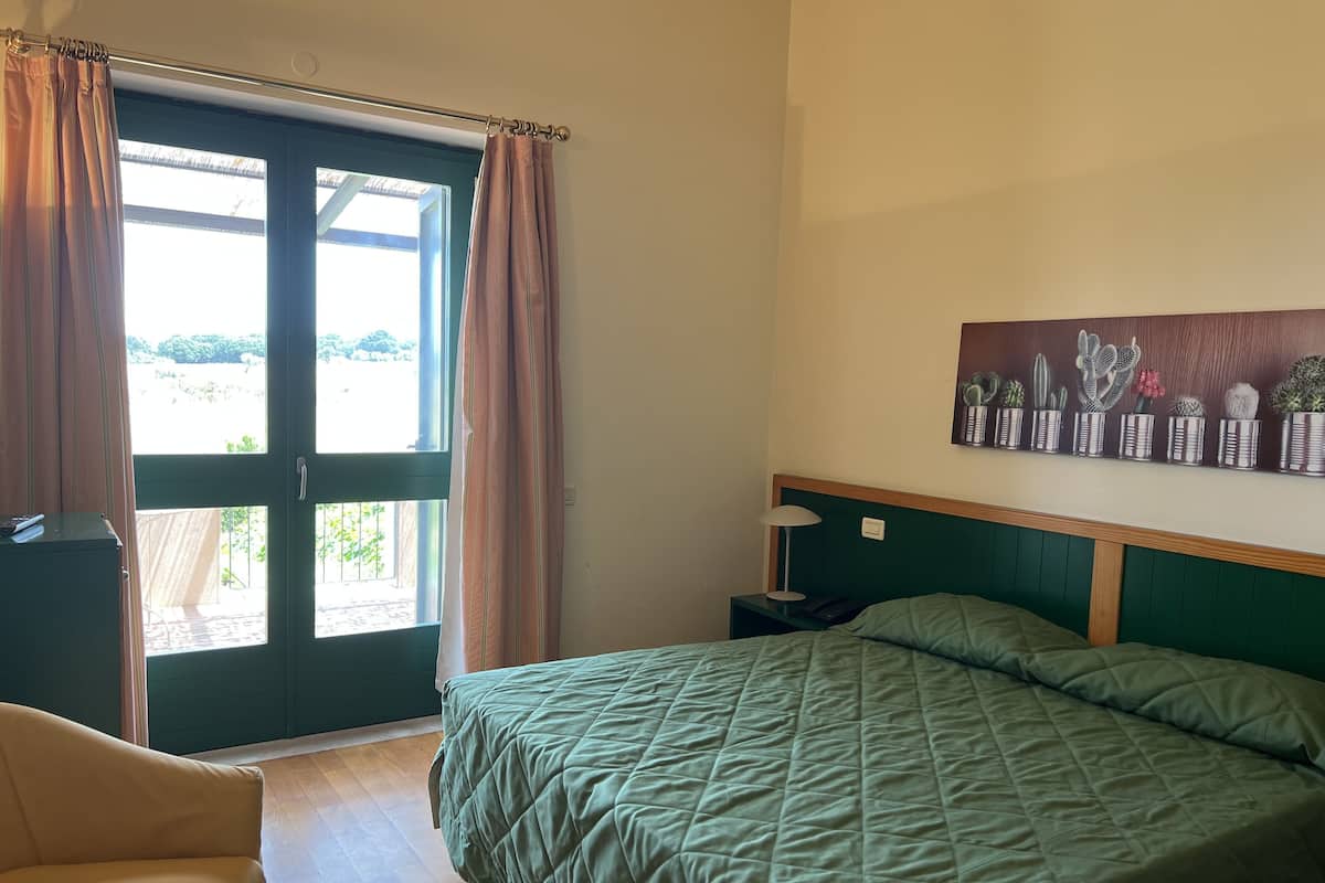 A bedroom with a bed, a chair, a nightstand, a lamp, and a window with curtains.