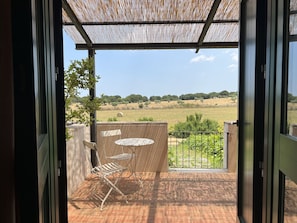 Een open balkon met uitzicht over een landelijk gebied, een tafel, twee stoelen en een pergola.