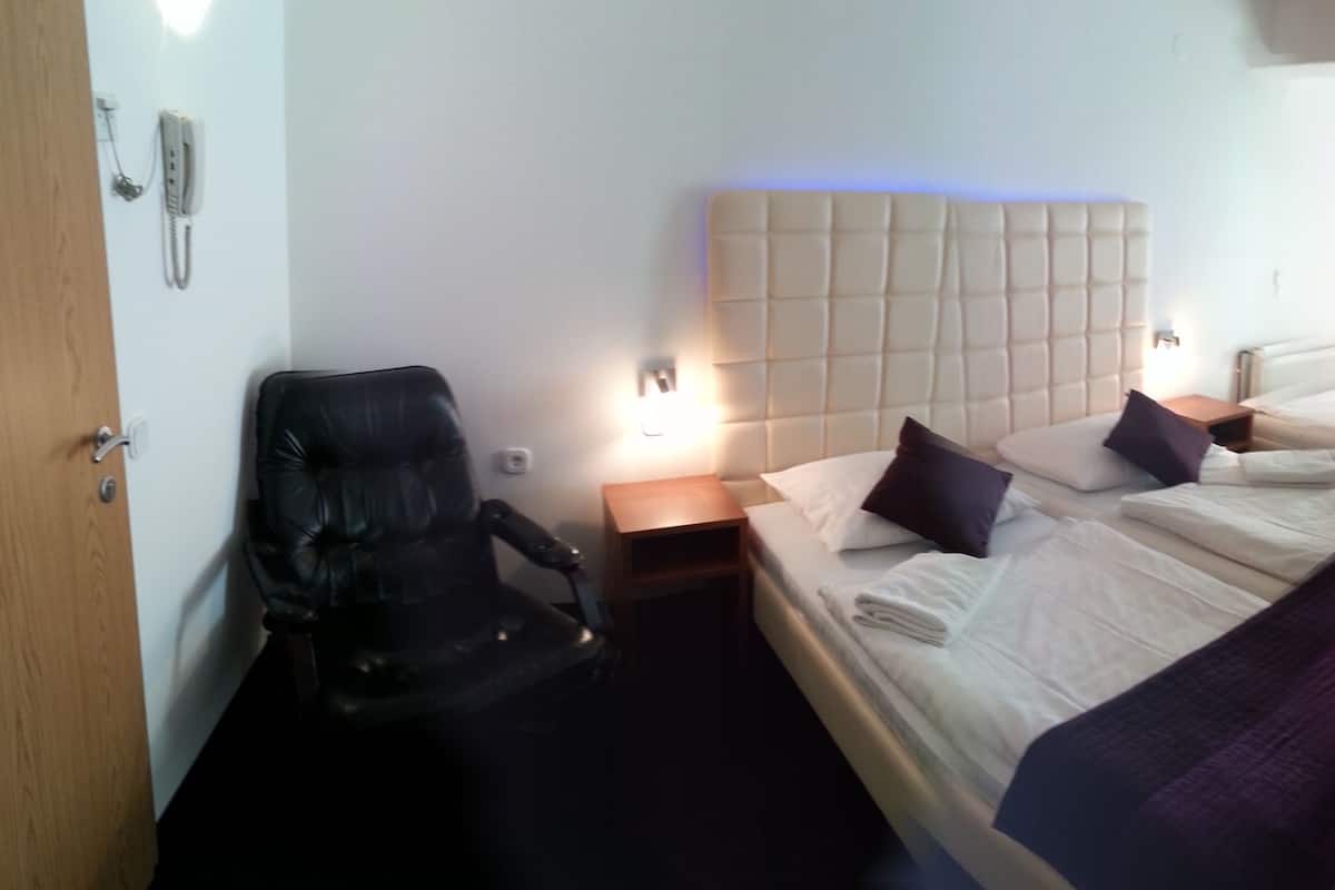 A hotel room with a bed, a chair, a bedside table, a lamp, and a mirror.