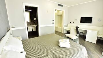 Habitación de hotel con cama, escritorio, silla, televisor y baño visible a través de una puerta abierta.