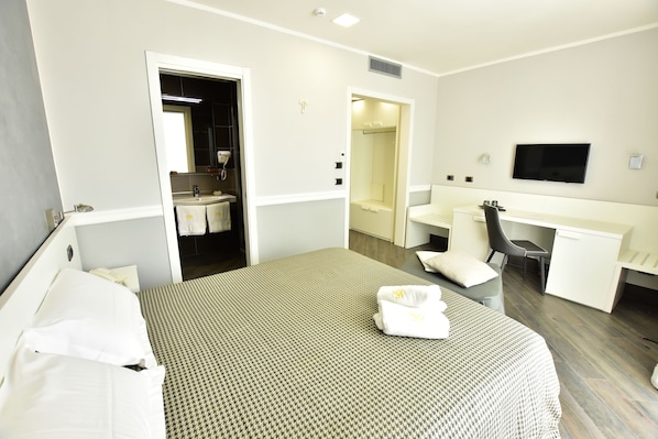 A hotel room with a bed, a desk, a chair, a TV, and a bathroom visible through an open door. - Palazzo Rosenthal Vesuview (Trecase)