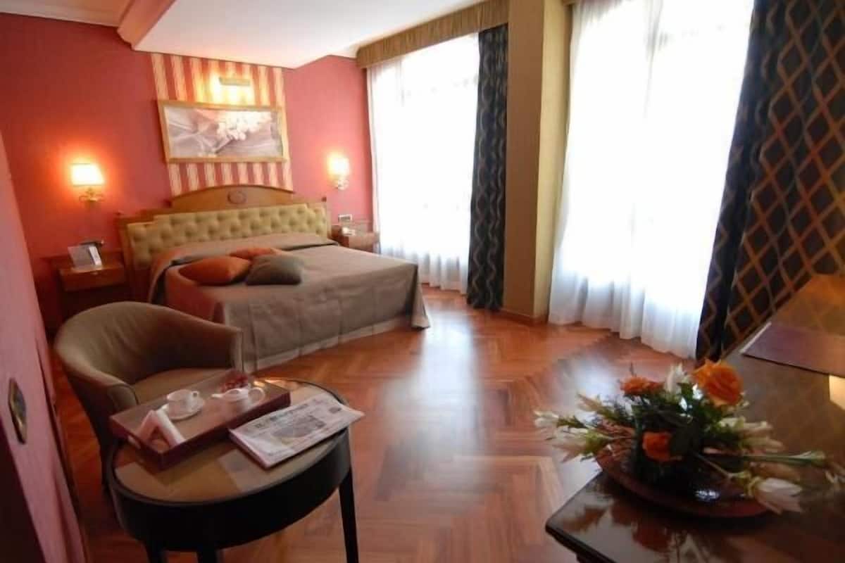 Een hotelkamer met een bed, een stoel, een tafel met een dienblad en een bloemenvaas.