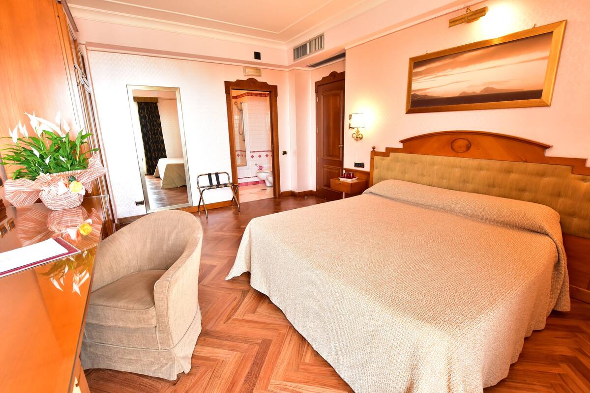 Een hotelkamer met een groot bed, een stoel, een bureau, een spiegel en een schilderij aan de muur.