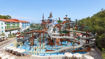 Parque acuático con múltiples toboganes y piscinas, rodeado de una zona de piscina con sombrillas y sillas reclinables.
