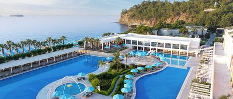 Un resort con una piscina grande, varias zonas de descanso y vistas al mar.