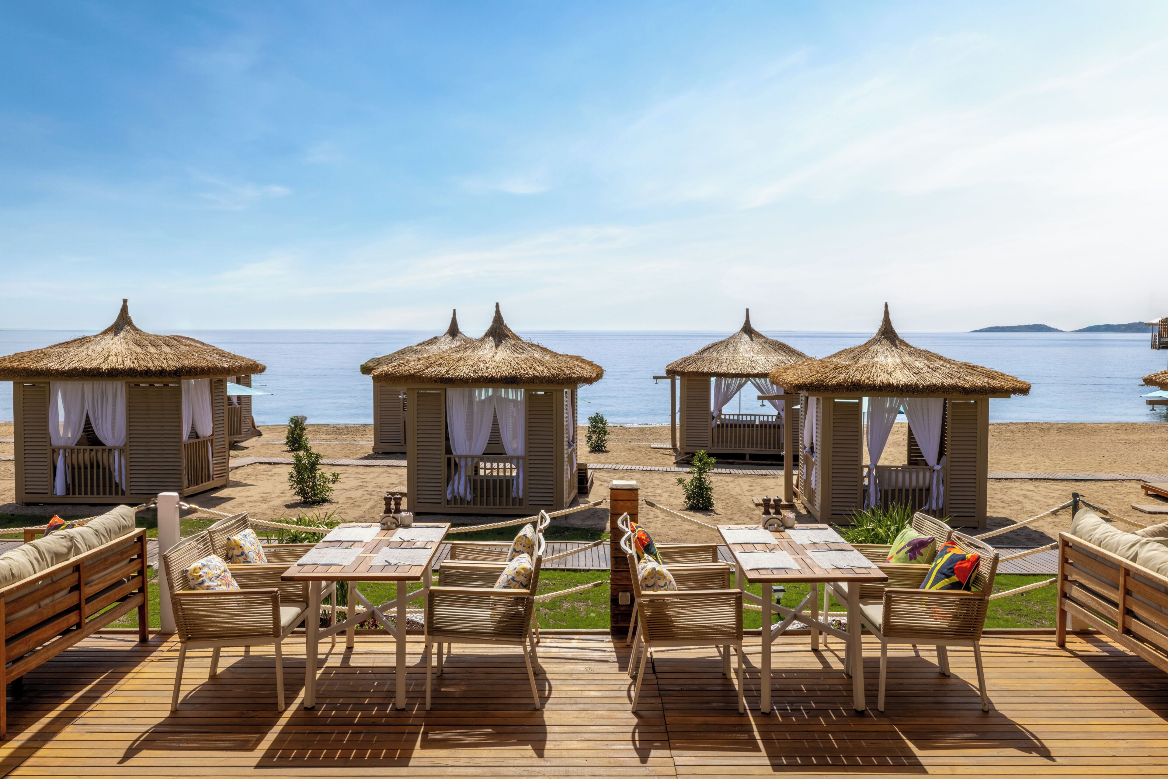 Un complexe hôtelier en bord de mer, doté de bungalows aux toits de chaume, de terrasses en bois et de tables.