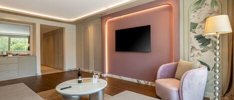A modern living room with a round coffee table, a comfortable armchair, and a flat-screen TV mounted on the wall.