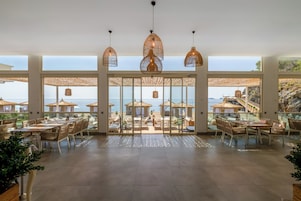 Un comedor amplio con ventanas grandes que dan a una playa, amoblado con mesas y sillas.