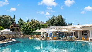 A swimming pool with lounge chairs and umbrellas, surrounded by greenery and a bar area. - Quinta do Paraíso (Lagoa)
