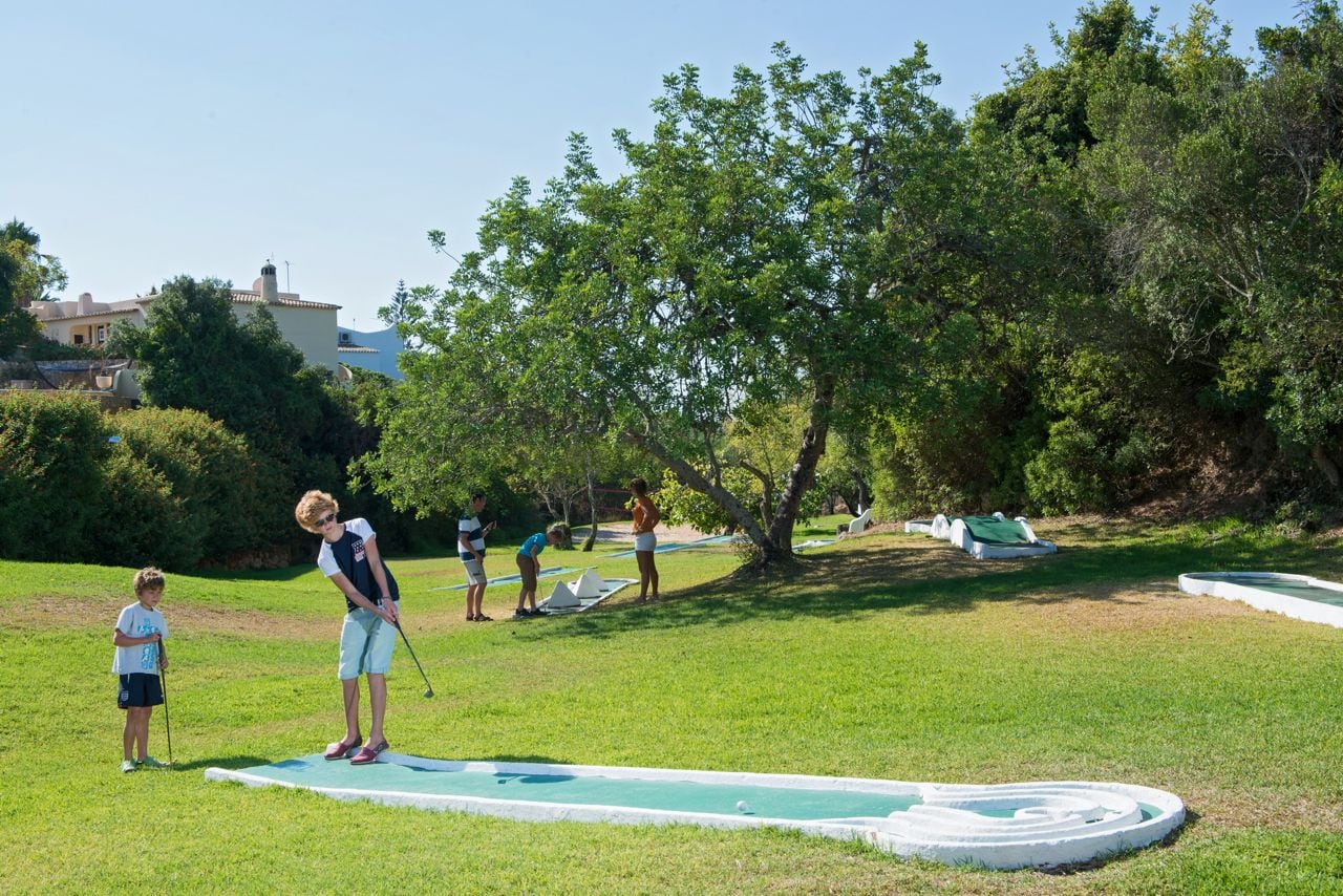Un campo de golf con un putting green, árboles y un edificio al fondo.
