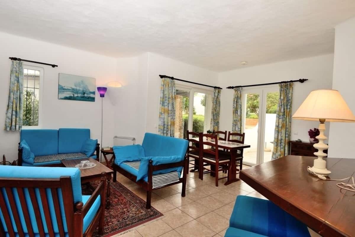 A room with a blue sofa, wooden dining table, chairs, and a lamp.
