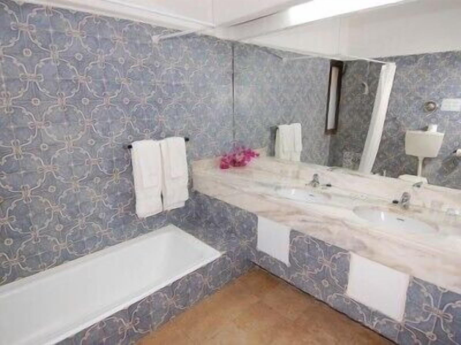 A bathroom with a marble vanity, two sinks, a bathtub, and patterned walls.