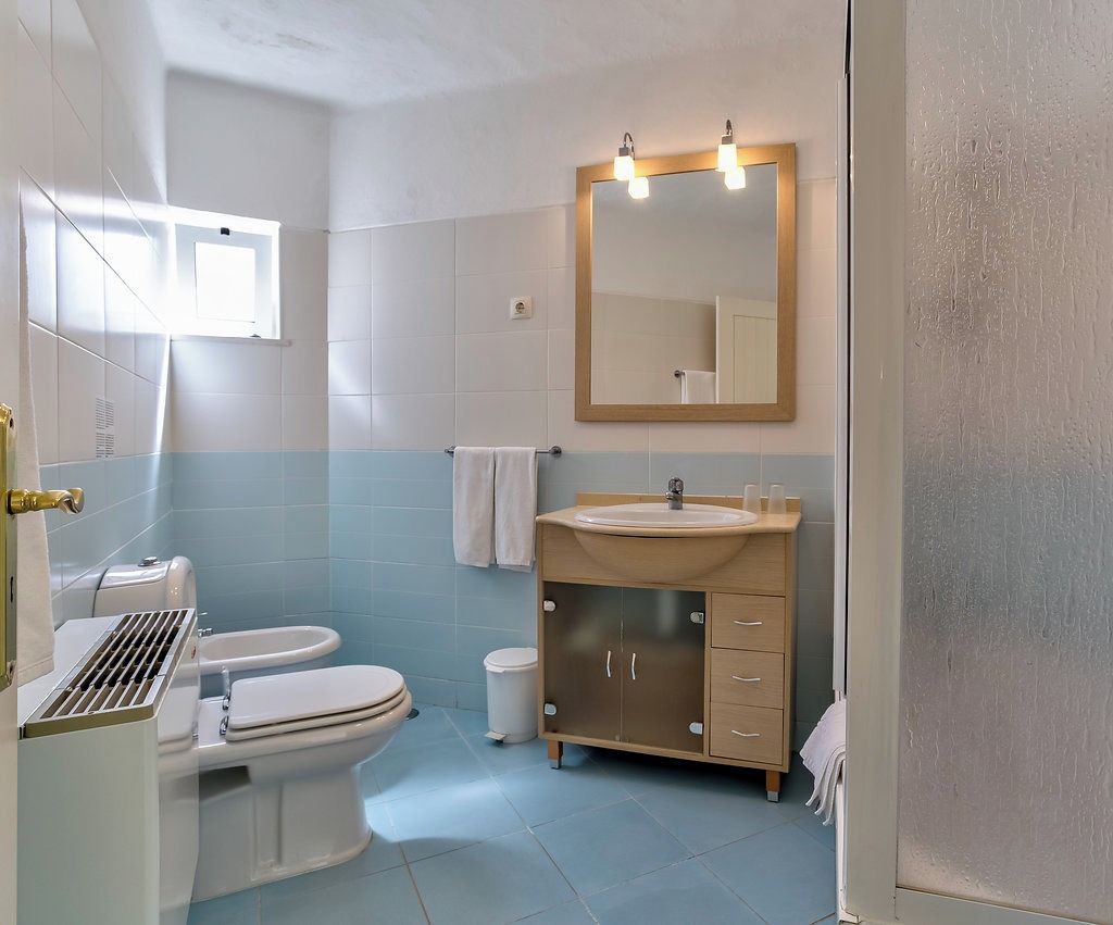 A bathroom with a toilet, sink, mirror, and a window.