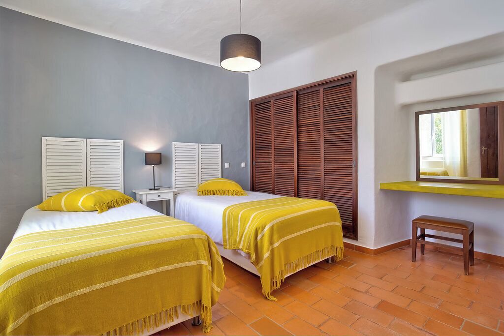 A room with two beds, a desk, a lamp, a window, and a wooden wardrobe.