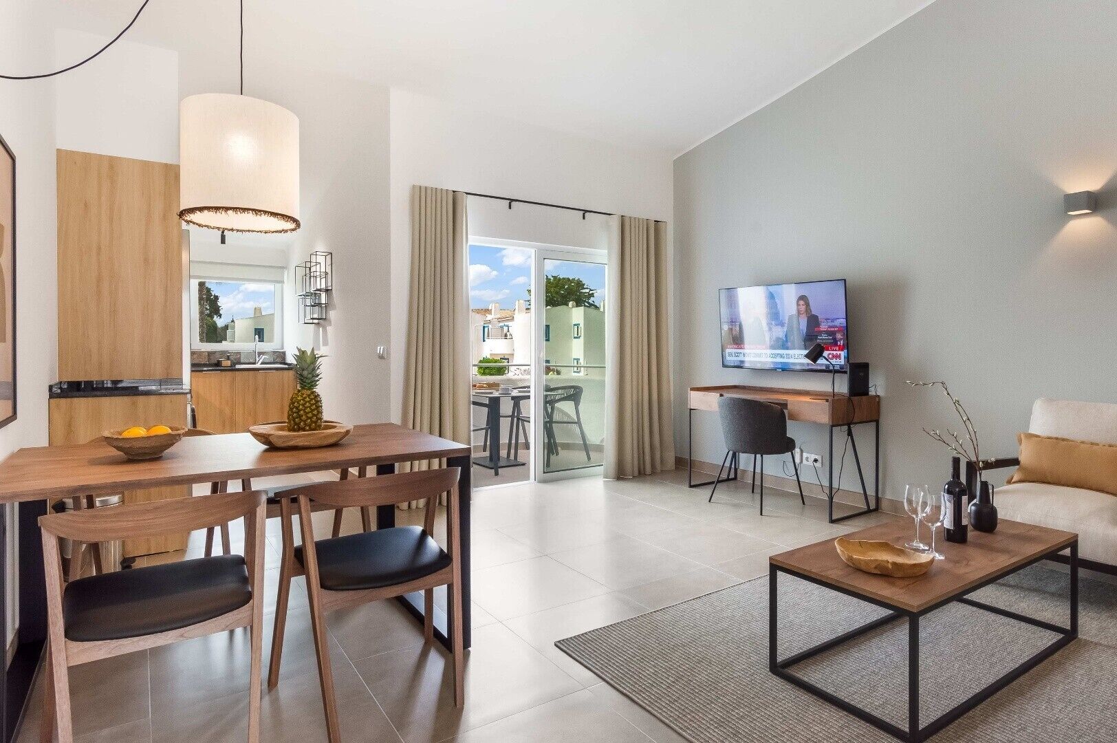 A modern living room with a dining area, a TV, and a kitchen visible through an open door.