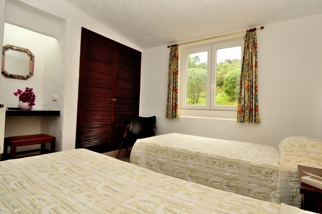 Une chambre avec deux lits, une armoire en bois, un miroir, une chaise et une fenêtre avec des rideaux.