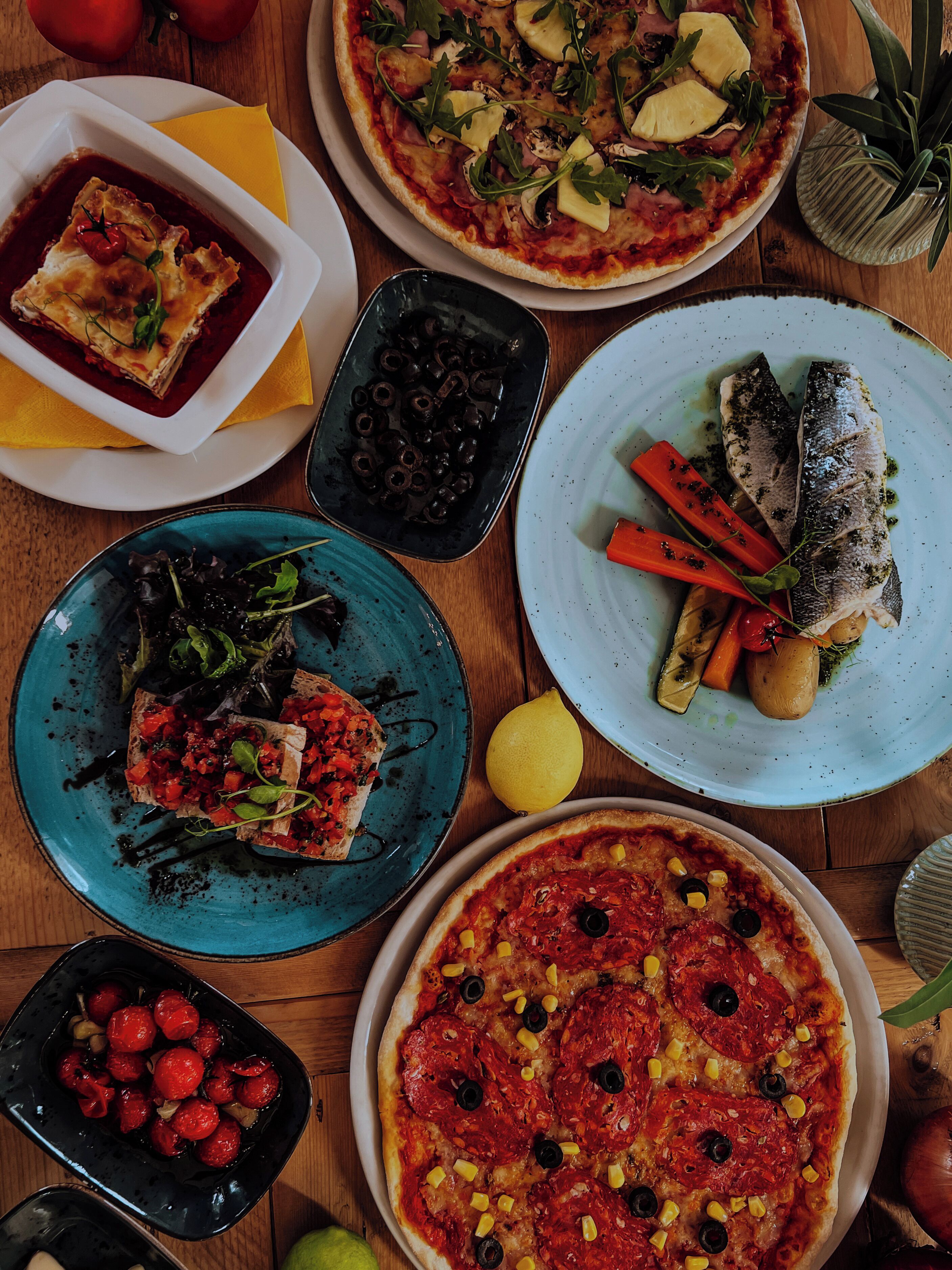 A variety of dishes including pizza, fish, and a salad, arranged on a wooden table.
