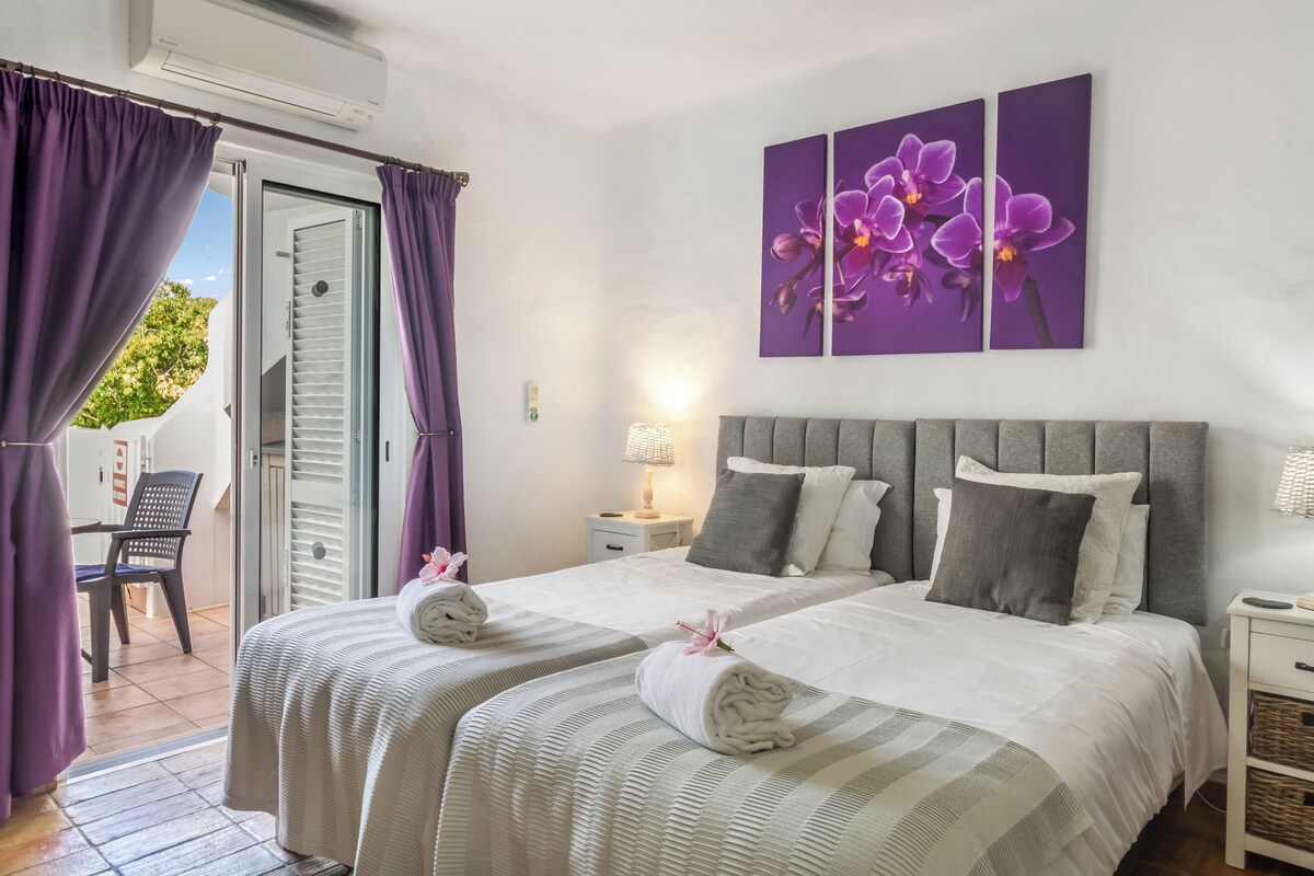 Habitación de hotel con dos camas, un balcón y cortinas moradas.
