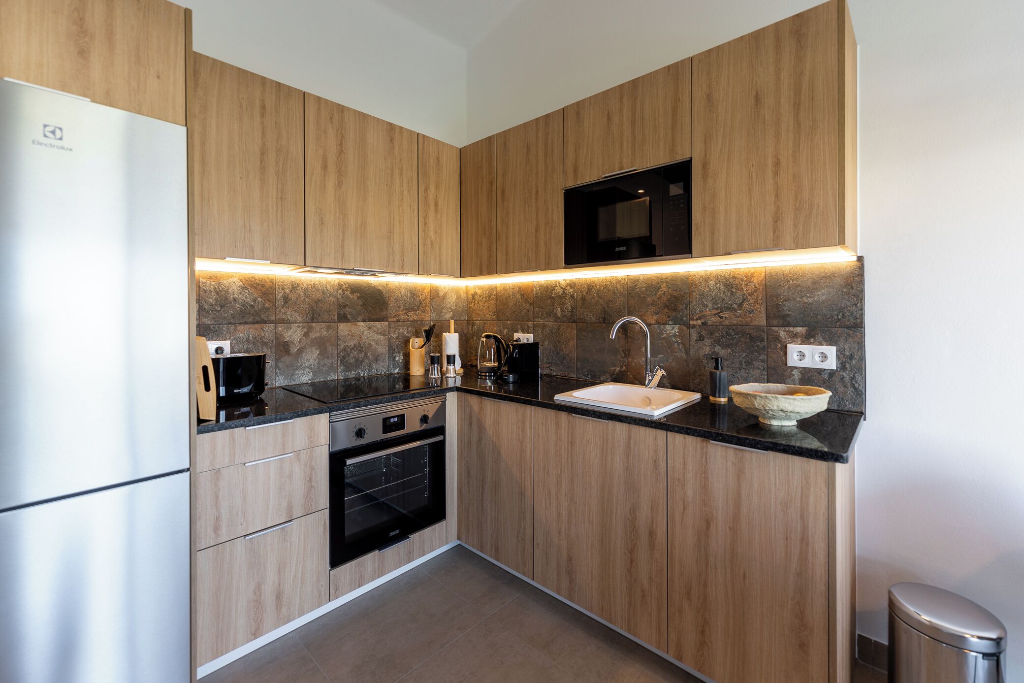 A modern kitchen with wooden cabinets, a built-in oven, a sink, and a microwave.