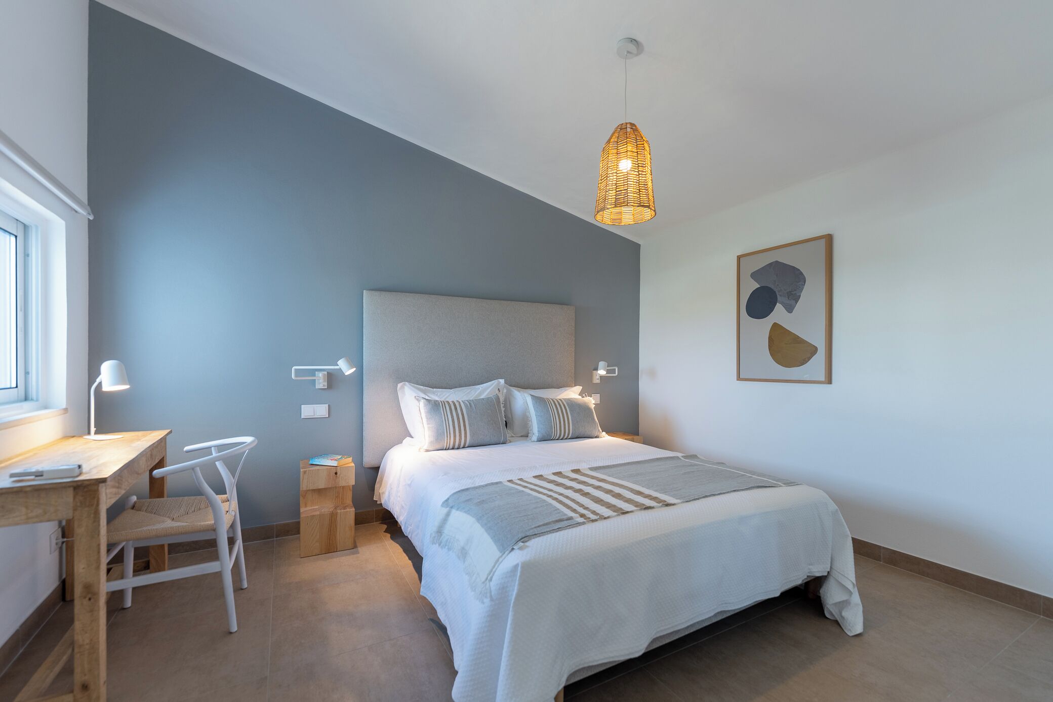 Ein Schlafzimmer mit einem Bett, Nachttischen, einem Schreibtisch, einem Sessel und einer Pendelleuchte.