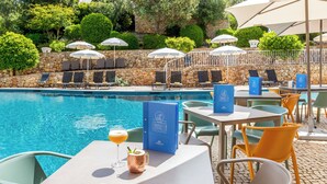 A poolside area with lounge chairs, umbrellas, and a table with a drink and a menu. - Quinta do Paraíso (Lagoa)